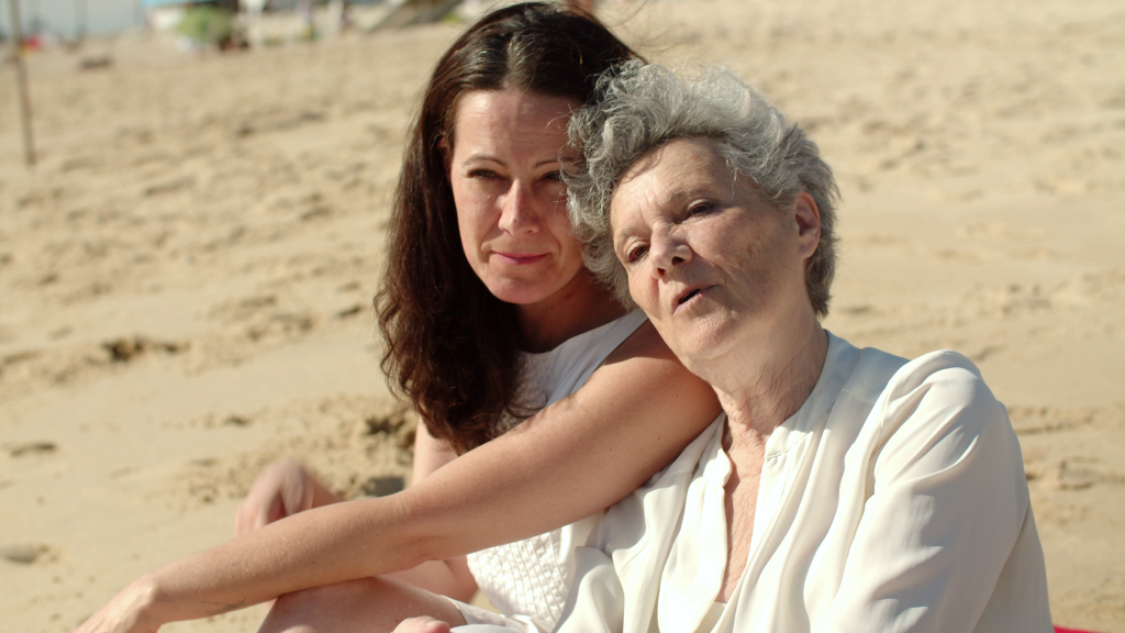 Two women, an adult and an elderly woman, enjoying a sunny beach, highlighting family connection at a senior living facility.