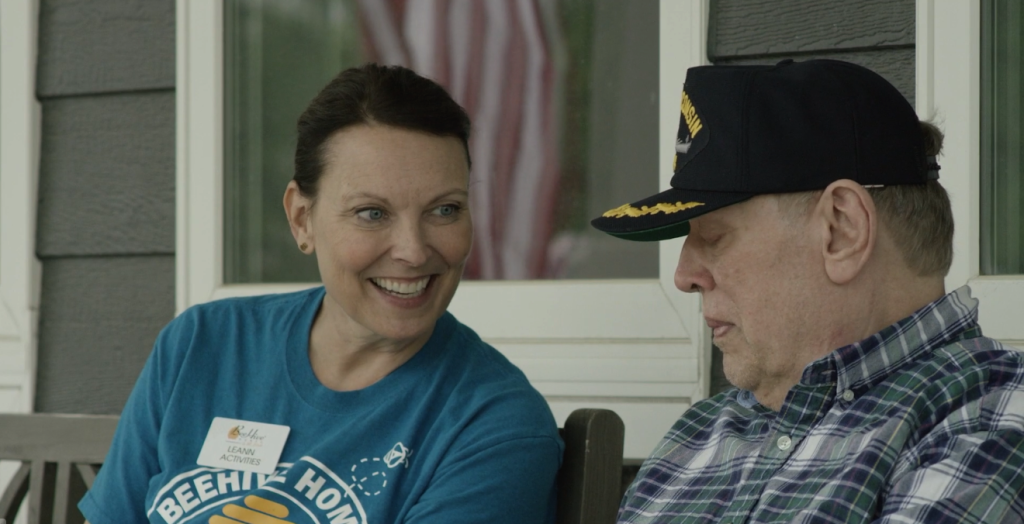 Smiling activity coordinator at BeeHive Homes engaging with a senior resident on a porch, highlighting compassionate care and community at the senior living facility in Rowlett, Texas.