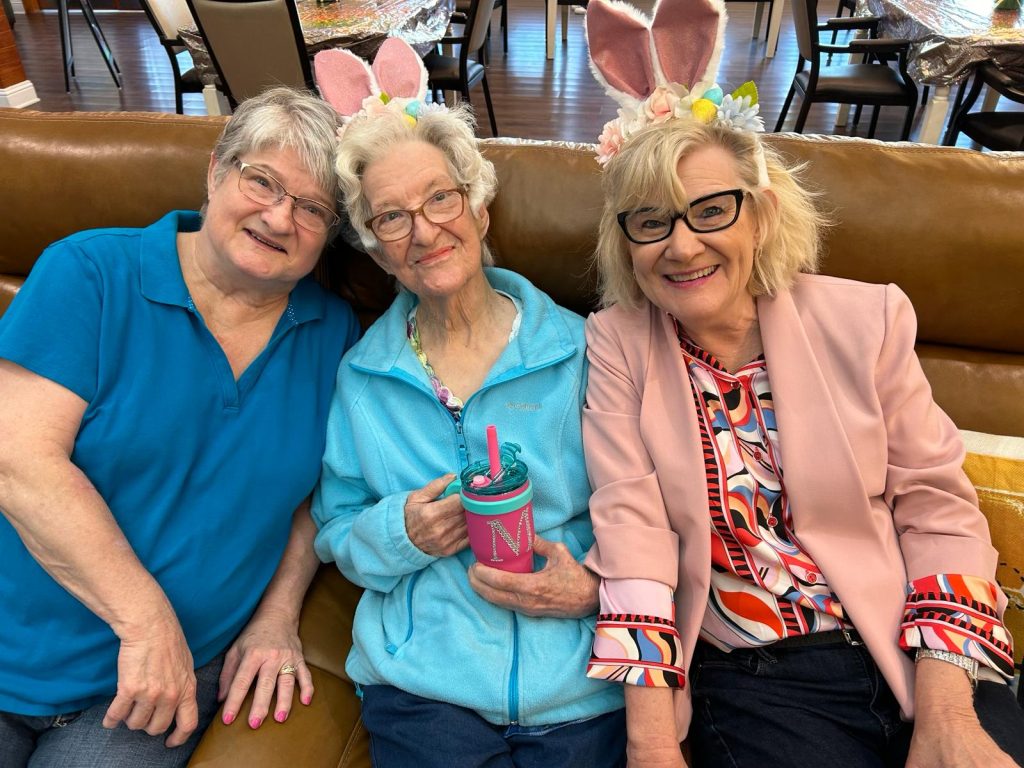 Three women wearing bunny ears celebrate with a colorful cup in a joyful atmosphere at BeeHive Homes of Rowlett.
